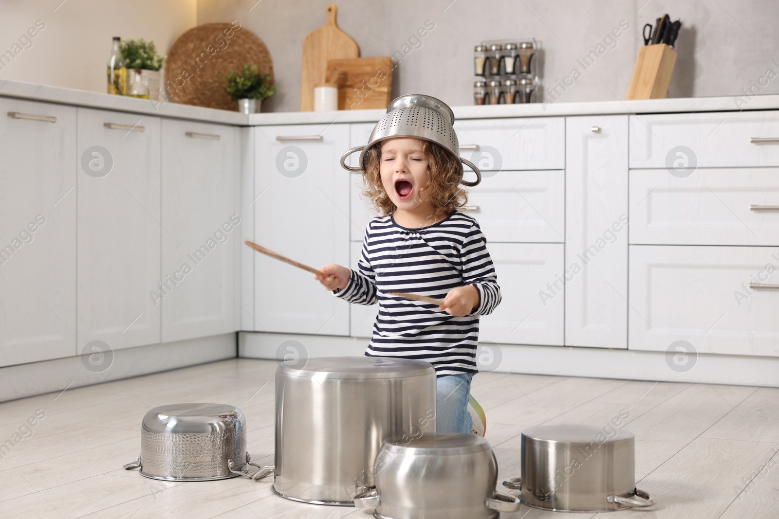 Photo of Little girl pretending to play drums on pots in kitchen