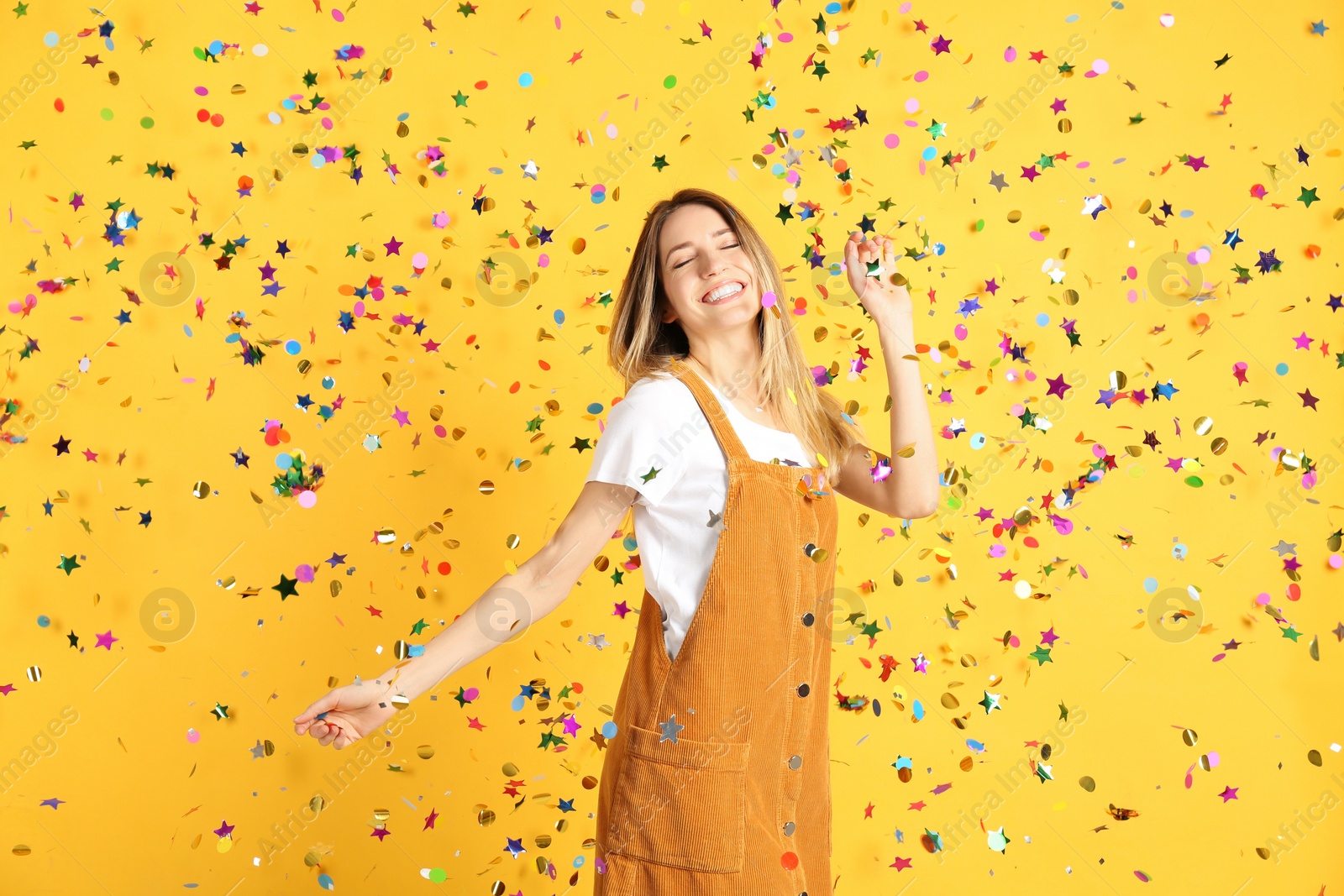 Photo of Happy woman and falling confetti on yellow background