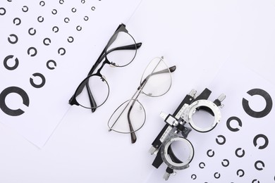 Vision test charts, glasses and trial frame on white background, flat lay