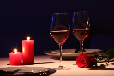 Photo of Beautiful table setting with glasses of wine, candles and rose in dark room. Romantic dinner for Valentine's day 