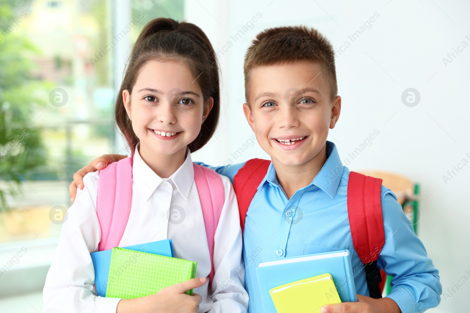 Photo of Cute little children with backpacks and school stationery in classroom