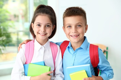 Cute little children with backpacks and school stationery in classroom