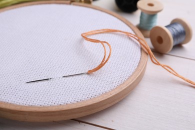 Photo of Embroidery hoop with fabric and needle on white wooden table, closeup