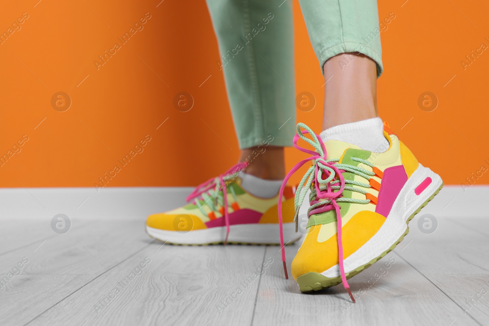 Photo of Woman wearing pair of new stylish sneakers near orange wall, closeup. Space for text