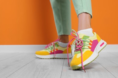 Woman wearing pair of new stylish sneakers near orange wall, closeup. Space for text