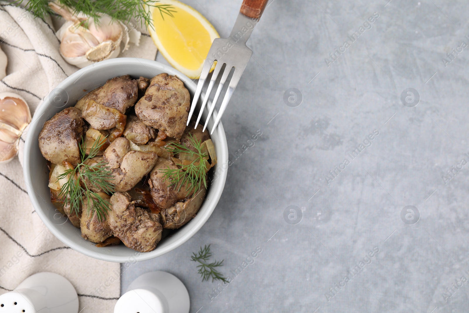 Photo of Tasty fried chicken liver with onion and dill served on grey table, flat lay. Space for text