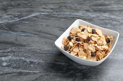 Photo of Bowl with cornflakes and raisins on dark table. Whole grain cereal for breakfast