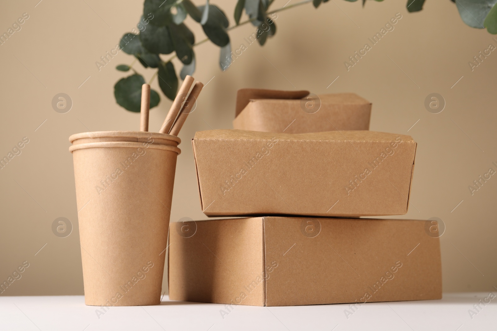 Photo of Eco friendly food packaging. Paper containers, straws and eucalyptus branches on white table against beige background