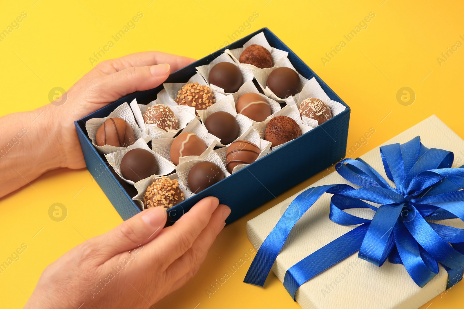 Photo of Woman with box of delicious chocolate candies on yellow background, closeup