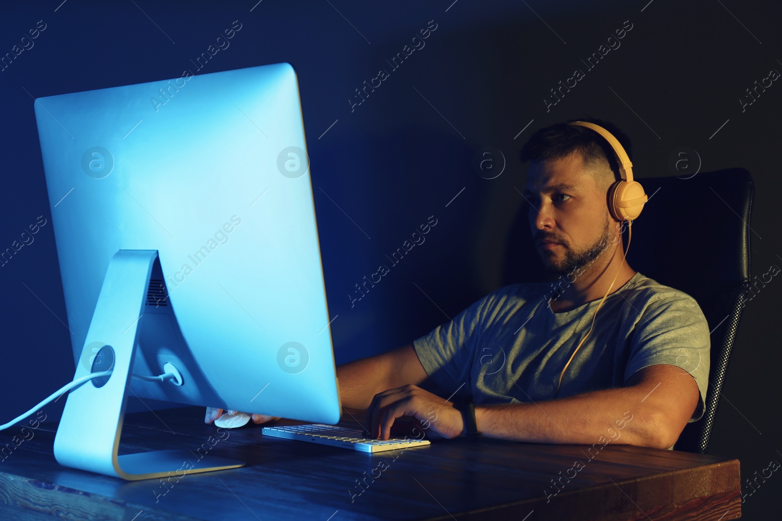 Photo of Man with headphones playing video game on modern computer in dark room