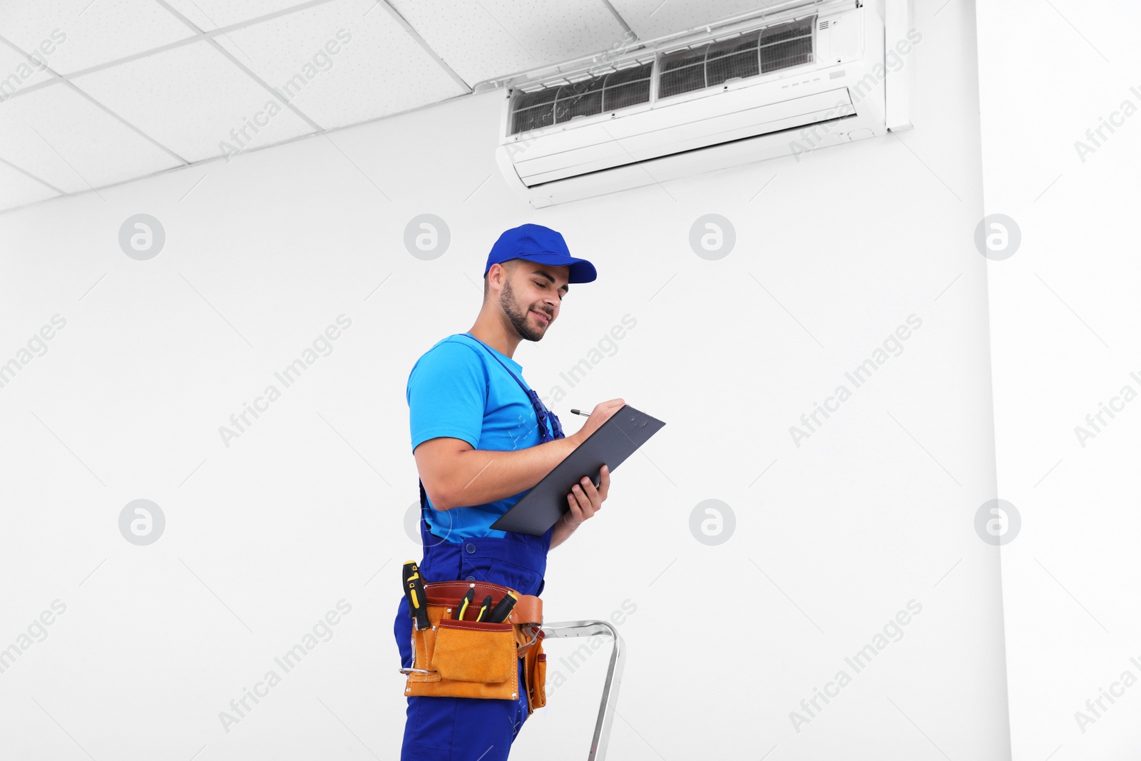 Photo of Professional technician with clipboard near modern air conditioner indoors