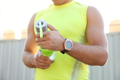 Photo of Man with fitness tracker and bottle of water after training outdoors, closeup