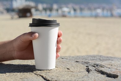 Photo of Woman with takeaway coffee cup on beach, closeup. Space for text