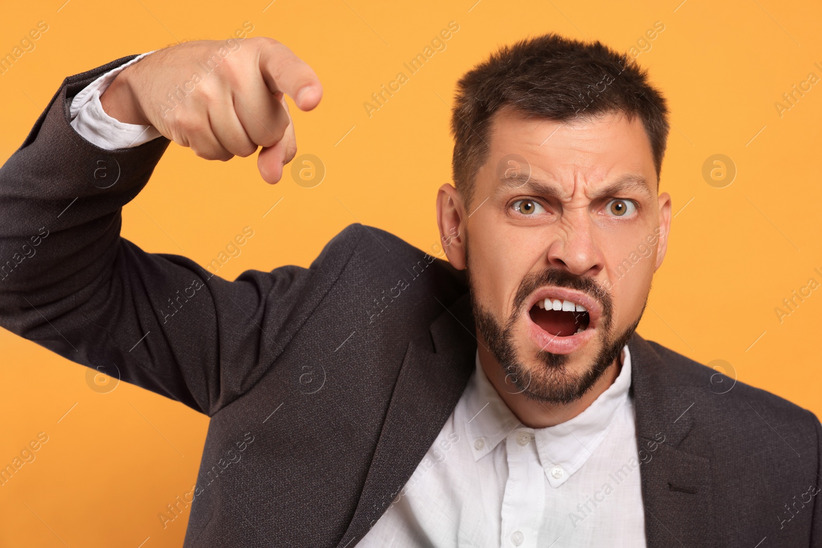 Photo of Aggressive man pointing on orange background. hate concept