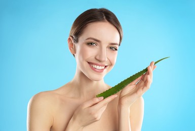 Photo of Happy young woman with aloe leaf on light blue background