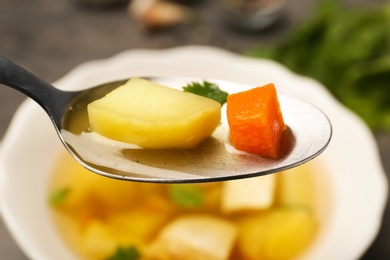 Photo of Spoon with fresh homemade chicken soup on blurred background, closeup