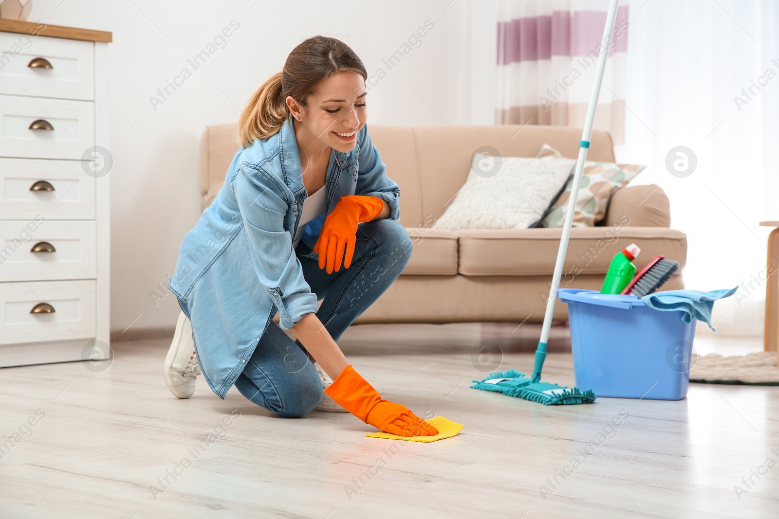 Photo of Young woman washing floor with rag and detergent in living room. Cleaning service