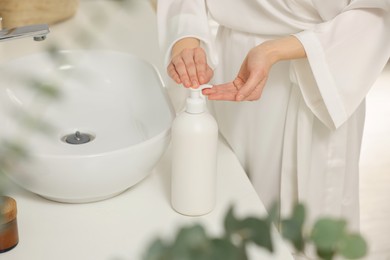 Young woman using body cream in bathroom, closeup