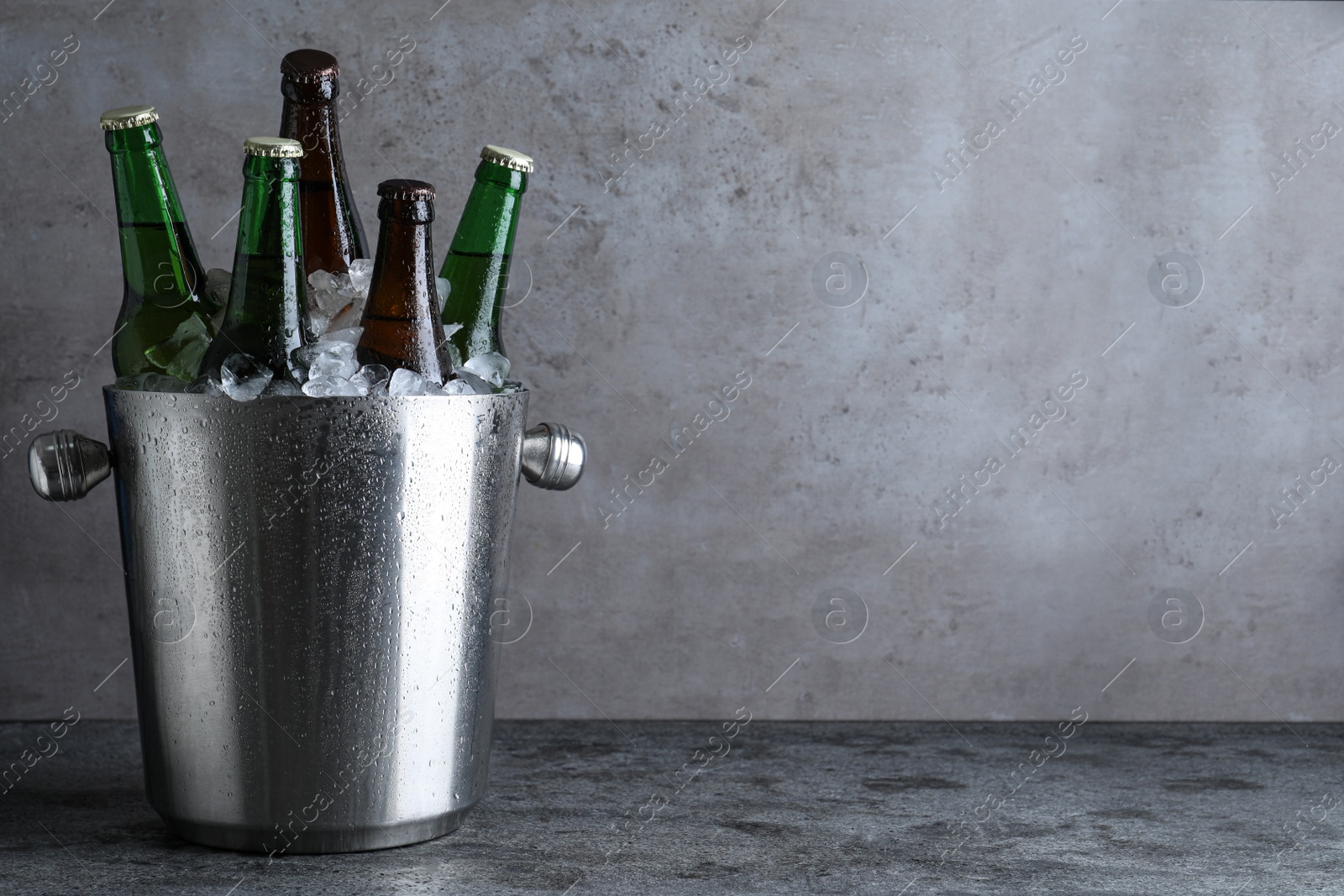 Photo of Metal bucket with bottles of beer and ice cubes on grey table, space for text