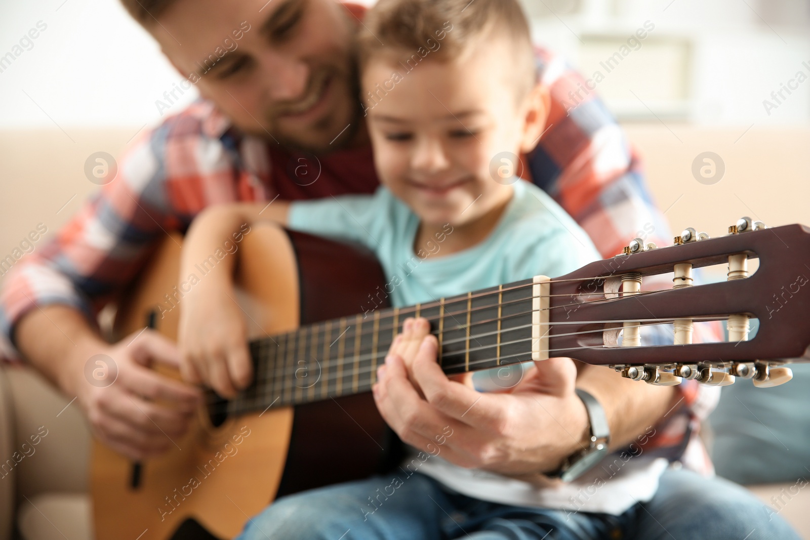 Photo of Father teaching his little son to play guitar at home