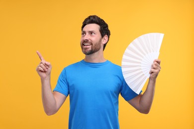 Happy man holding hand fan on orange background