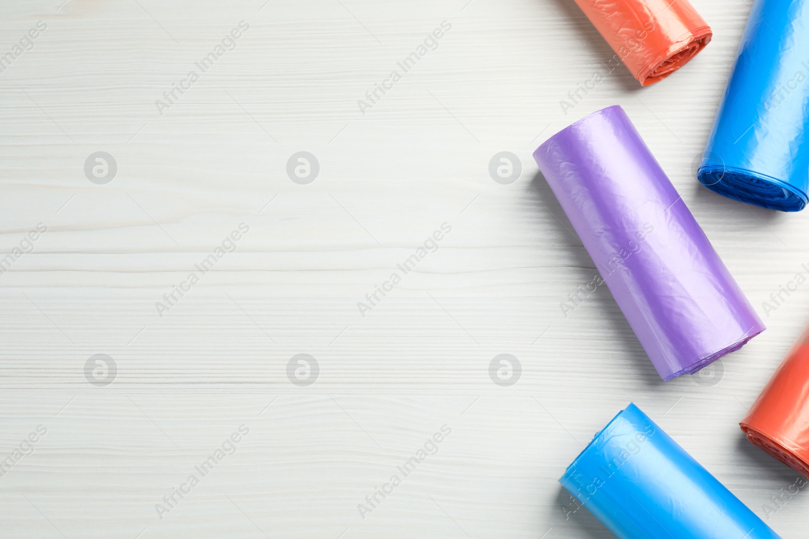Photo of Rolls of different color garbage bags on white wooden table, flat lay. Space for text