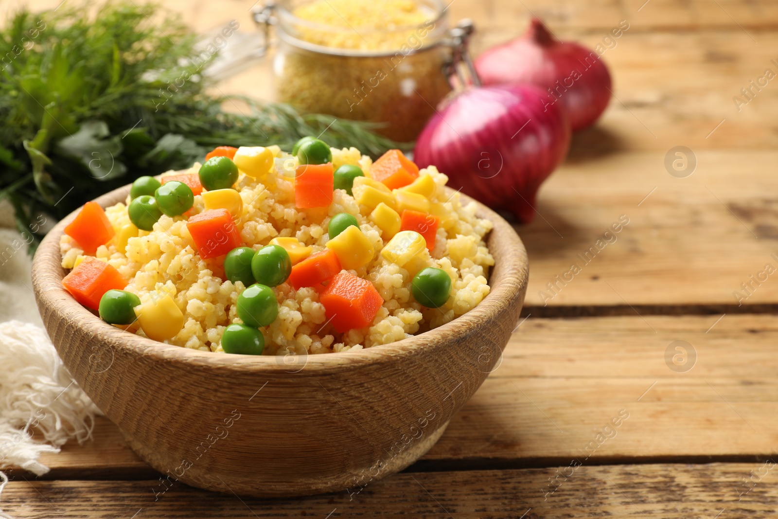 Photo of Tasty millet porridge with vegetables in bowl on wooden table, closeup. Space for text