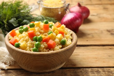 Photo of Tasty millet porridge with vegetables in bowl on wooden table, closeup. Space for text