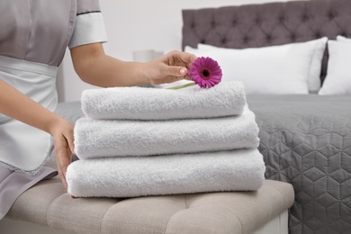 Maid with fresh towels and flower in hotel room, closeup