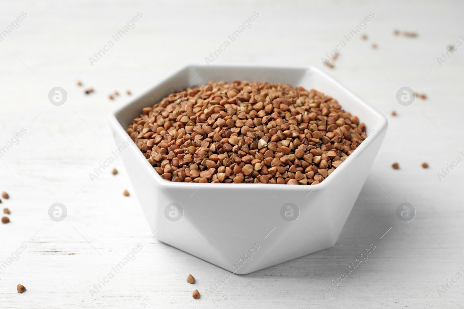 Photo of Uncooked buckwheat in bowl on wooden table