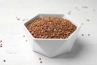 Uncooked buckwheat in bowl on wooden table