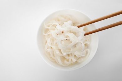 Photo of Rice noodles on chopsticks over bowl against white background, top view