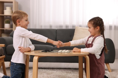 Happy children shaking hands after playing checkers at coffee table in room