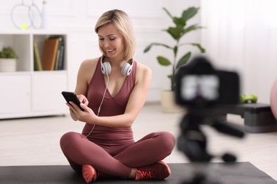 Smiling sports blogger recording fitness lesson with camera at home