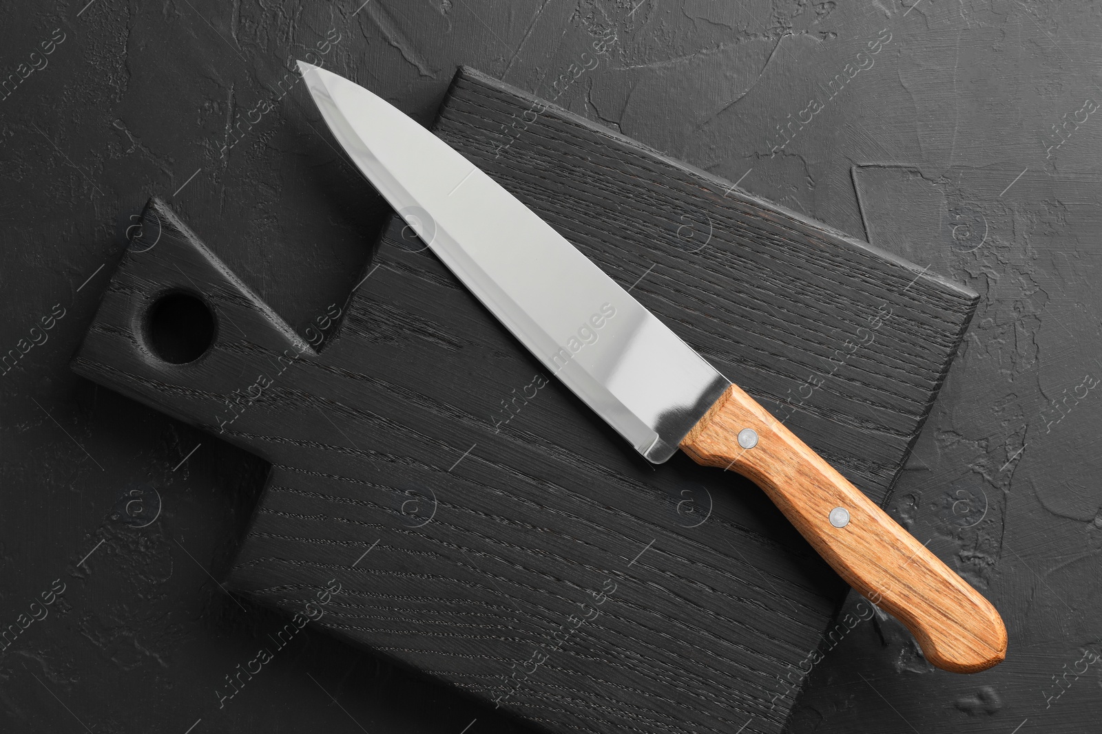 Photo of One sharp knife and board on dark textured table, top view