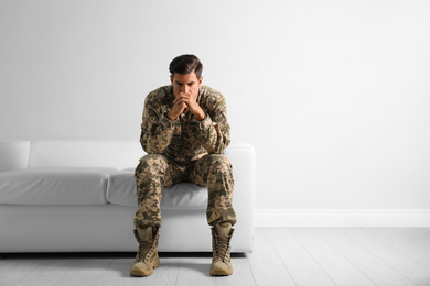 Photo of Stressed military officer sitting on sofa near white wall indoors. Space for text