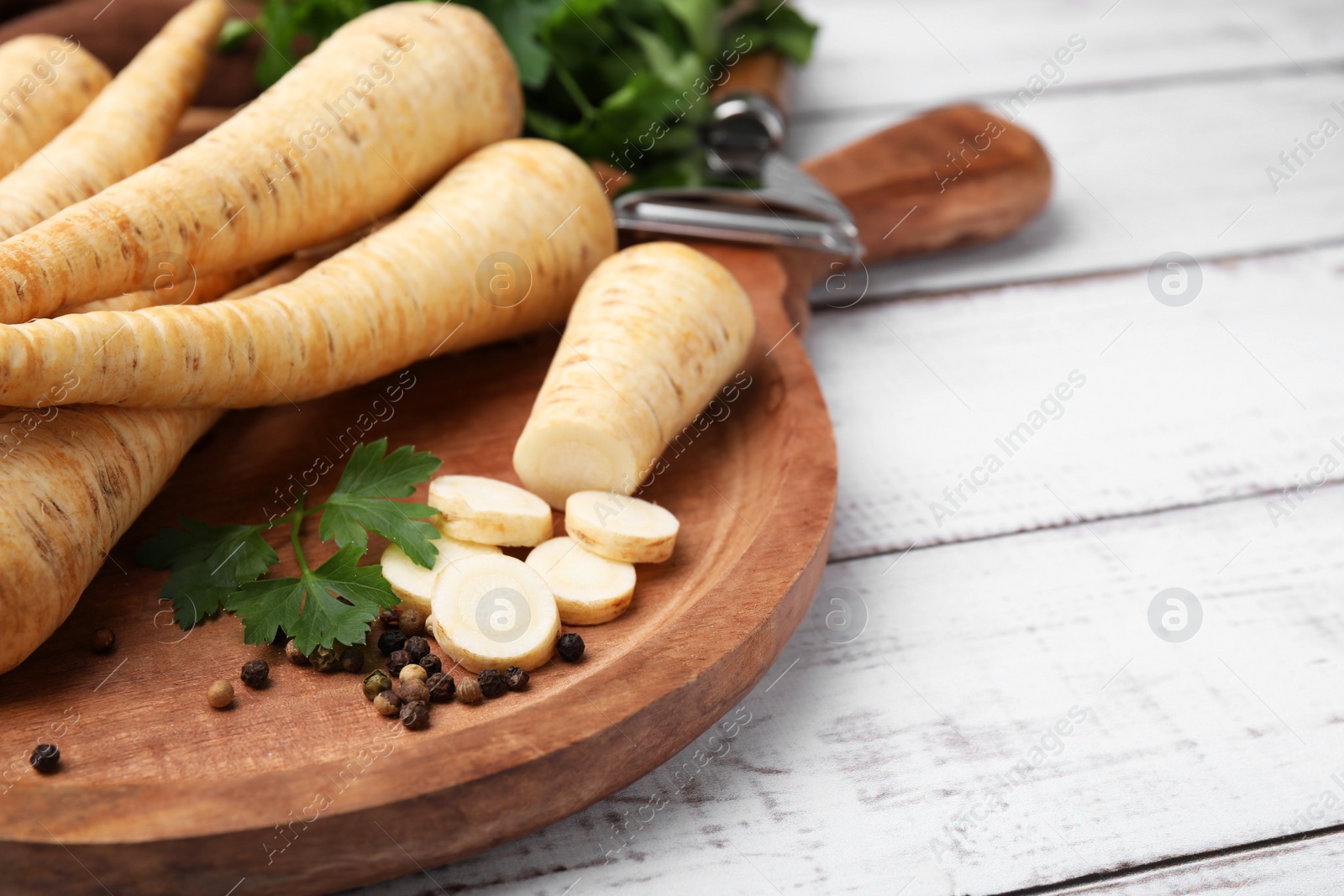 Photo of Raw parsley roots and fresh herb on white wooden table, closeup. Space for text