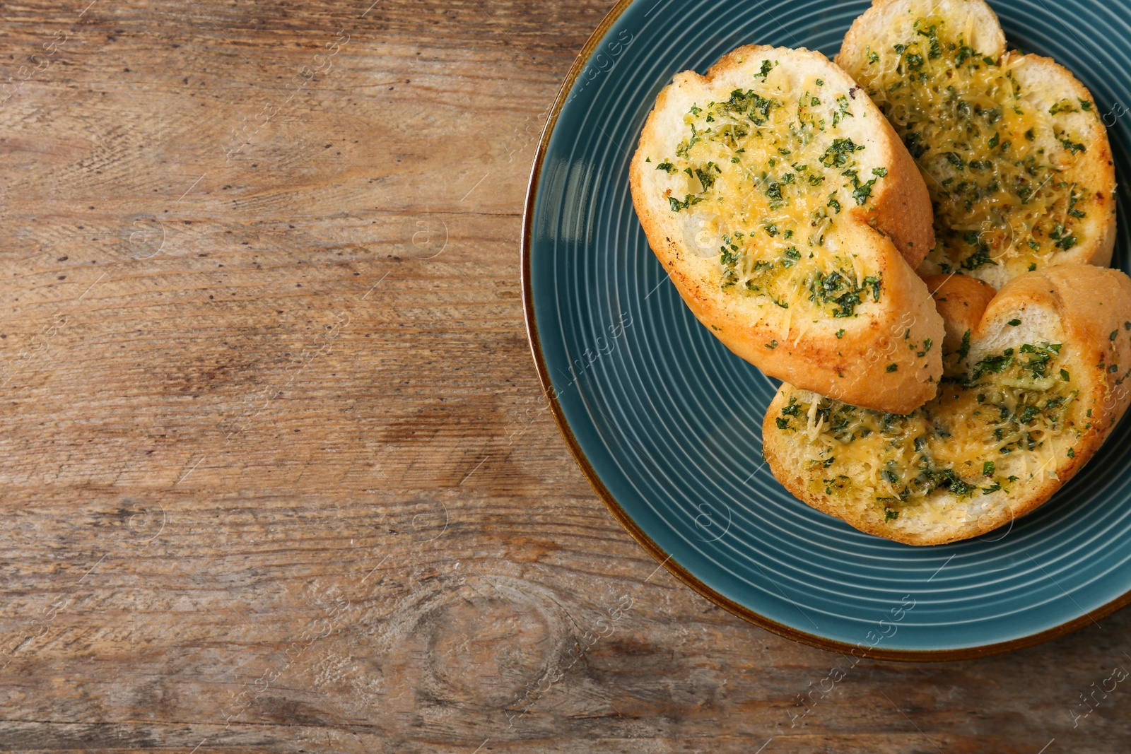 Photo of Slices of toasted bread with garlic, cheese and herbs on wooden table, top view. Space for text