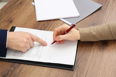 Man pointing at document and woman putting signature at wooden table, closeup