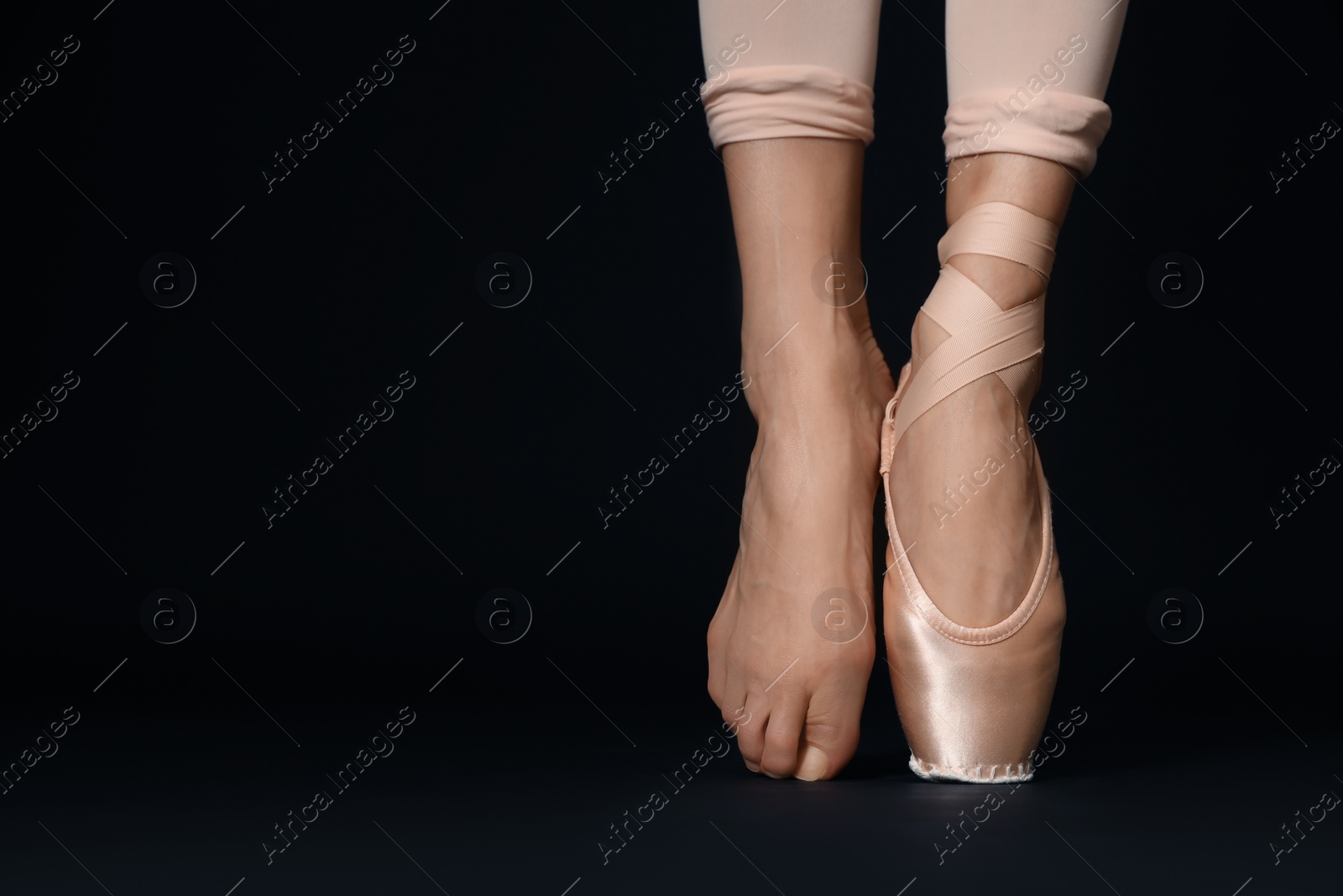 Photo of Ballerina in pointe shoe dancing on black background, closeup. Space for text