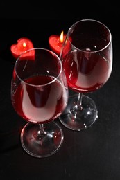 Photo of Glasses of wine and heart shaped candles for romantic dinner on black table