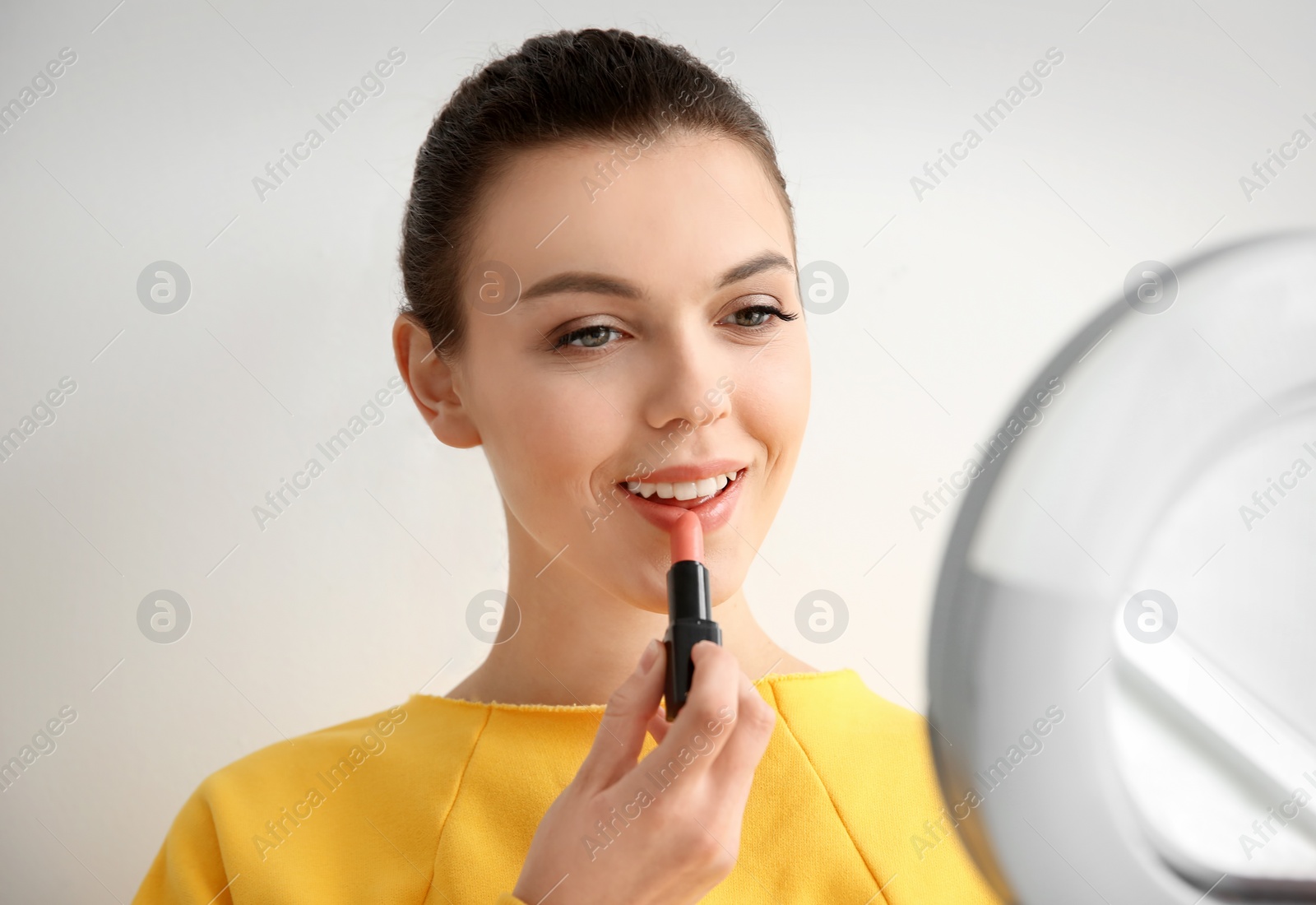 Photo of Young woman applying lipstick on light background. Professional makeup products