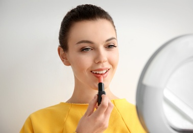 Photo of Young woman applying lipstick on light background. Professional makeup products