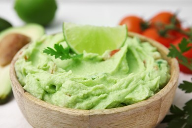 Photo of Bowl of delicious guacamole with lime, closeup