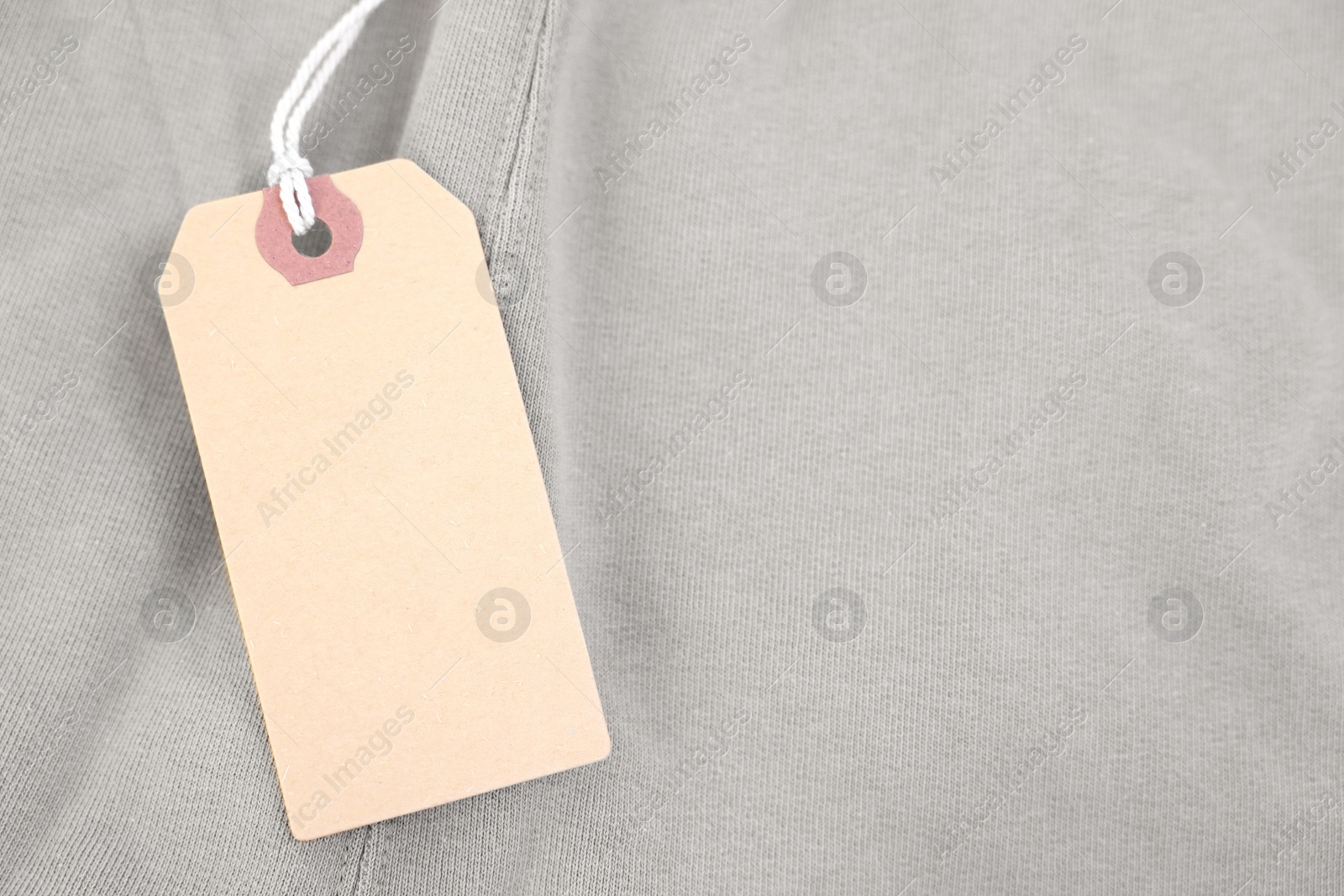 Photo of Cardboard tag on beige garment, top view. Space for text