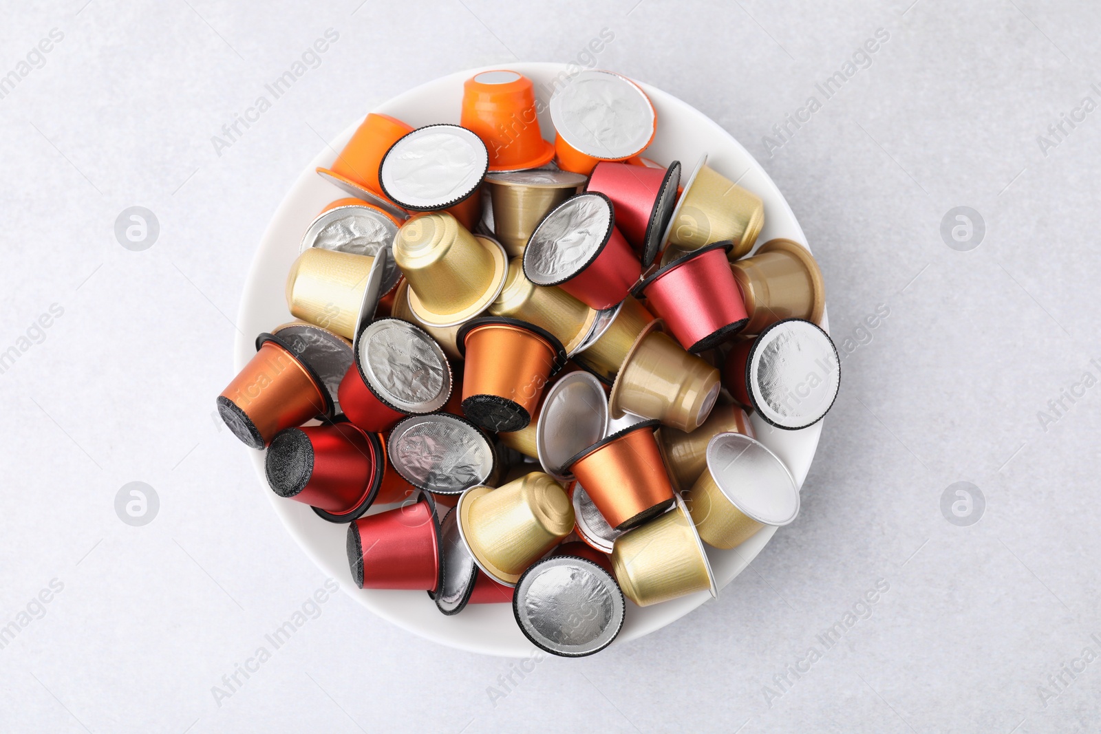 Photo of Bowl of many coffee capsules on light grey table, top view