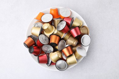 Photo of Bowl of many coffee capsules on light grey table, top view