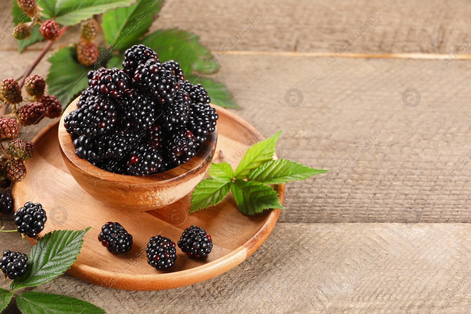 Photo of Fresh ripe blackberries and leaves on wooden table. Space for text