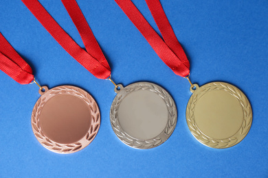 Photo of Gold, silver and bronze medals on blue background, flat lay. Space for design