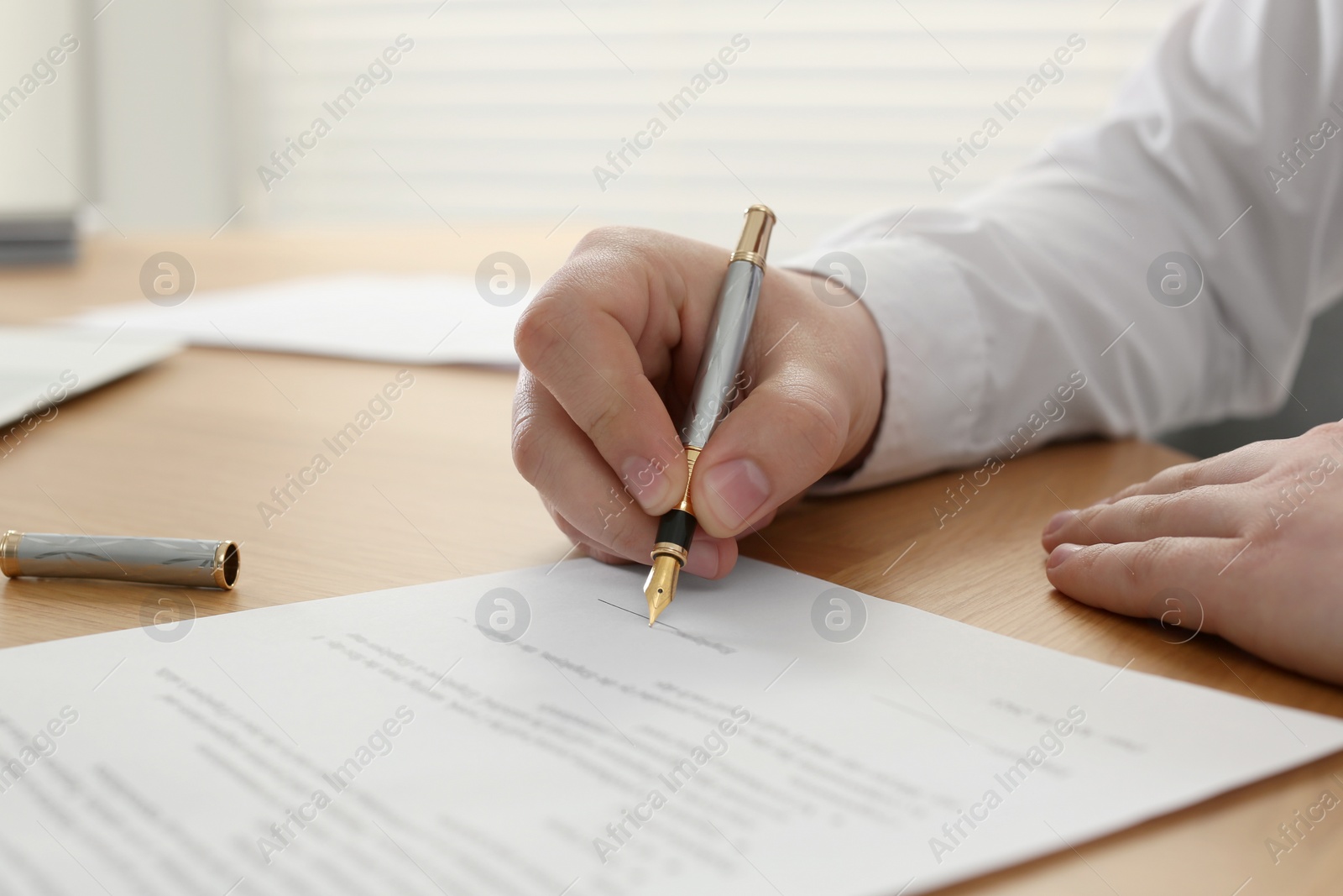 Photo of Notary signing document at wooden table indoors, closeup